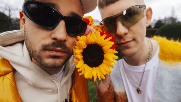 DJ duo DJ Heartstring, ruikend aan een zonnebloem met zonnebrillen op.